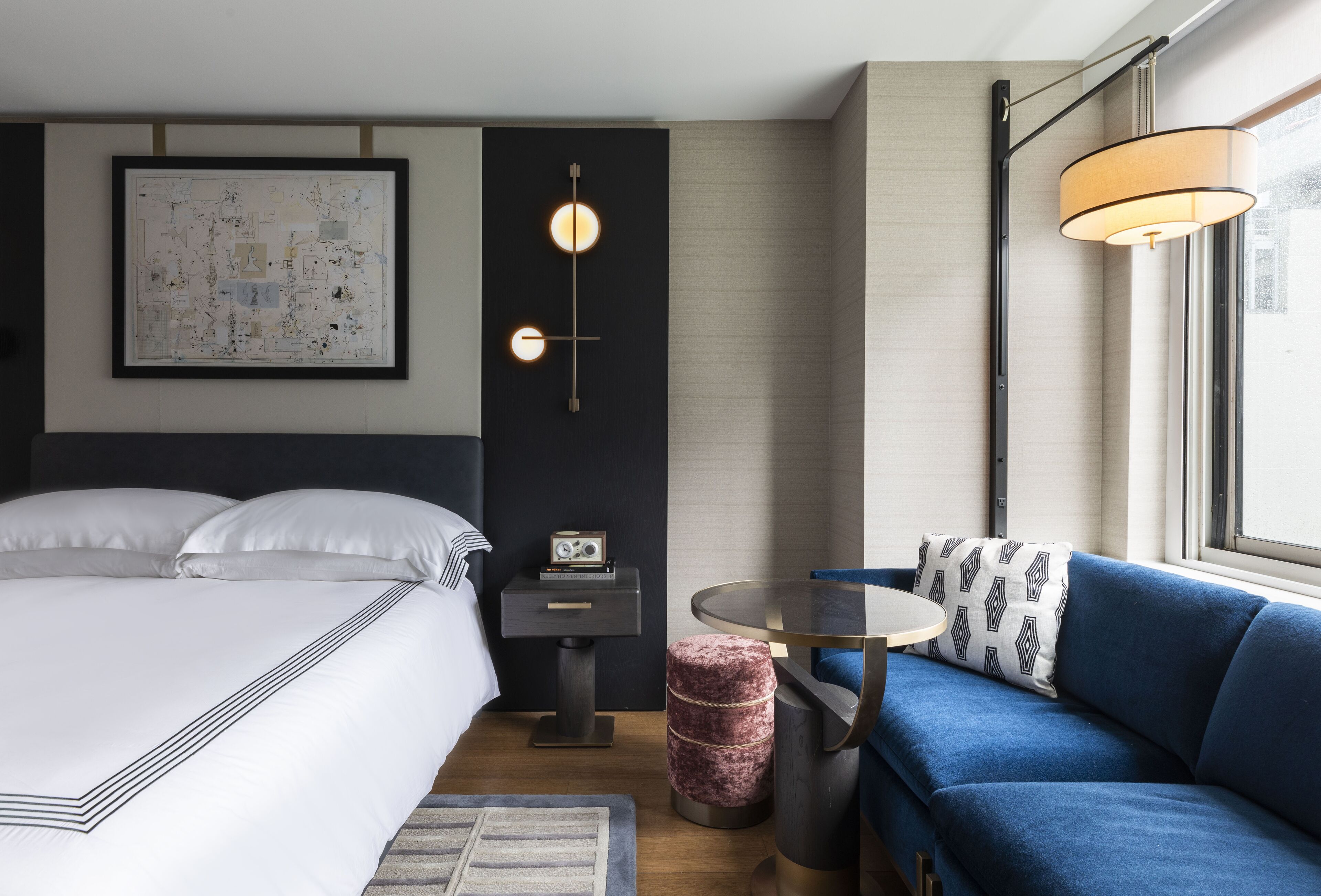 Ett modernt hotellrum med en stor säng, en blå soffa, ett litet runt bord och en väggmonterad lampa.
