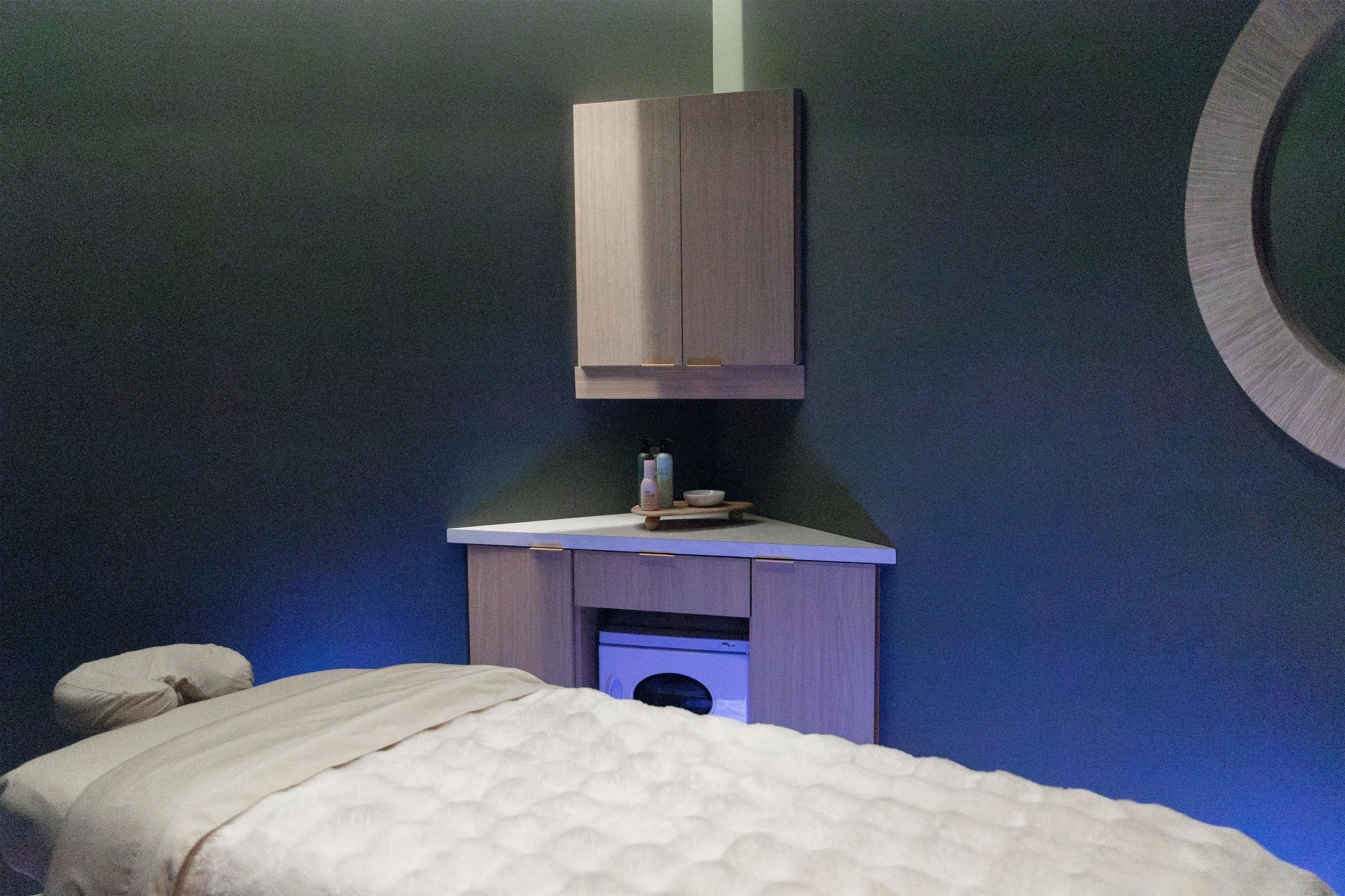 A room with a bed, a small table with toiletries, and a wall-mounted cabinet.