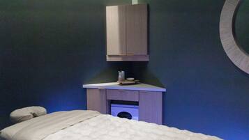 A room with a bed, a small table with toiletries, and a wall-mounted cabinet.