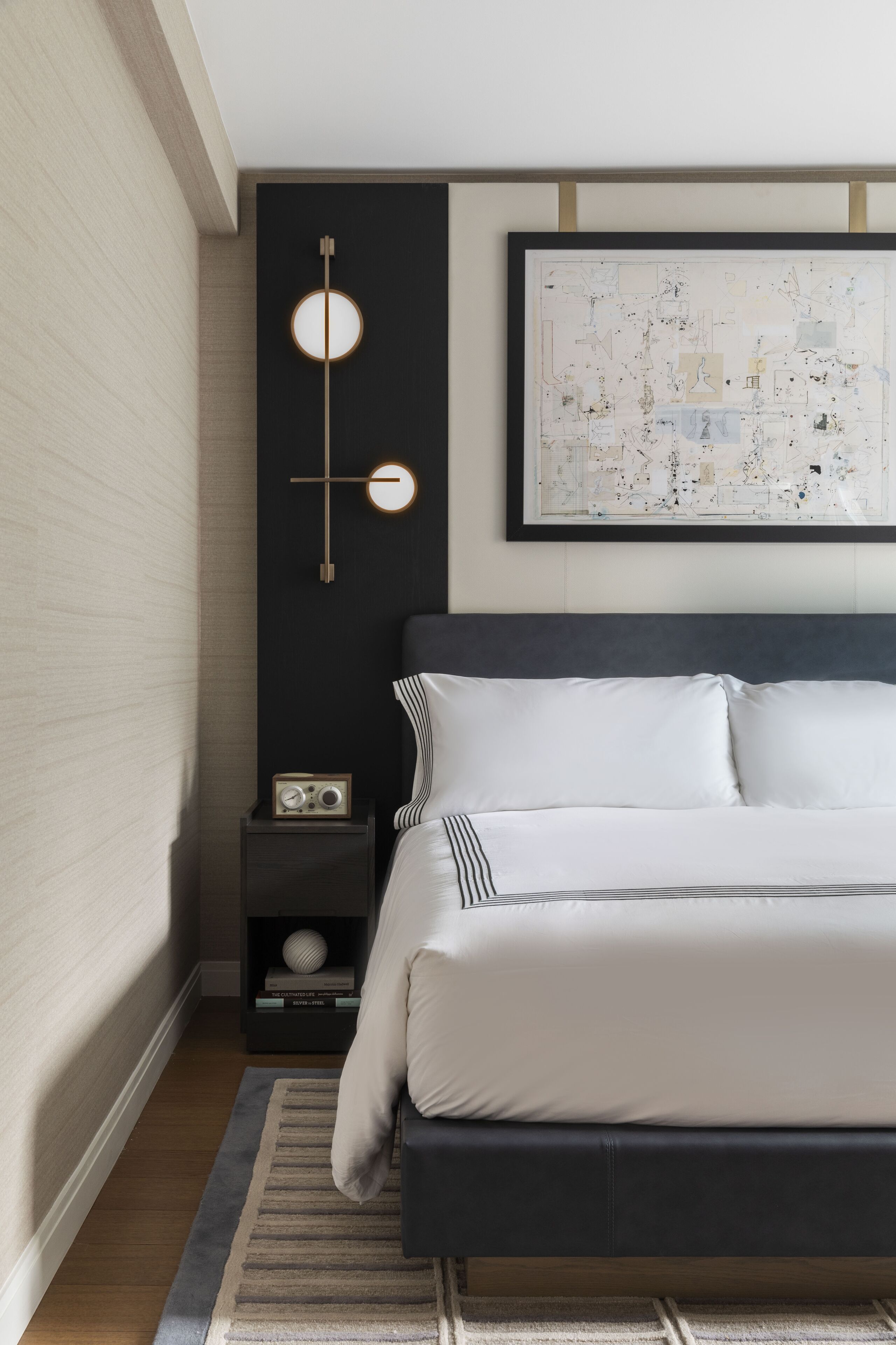 Una camera da letto moderna con un letto grande, un portalume a parete, una mappa astratta incorniciata e un piccolo comodino con una radio.