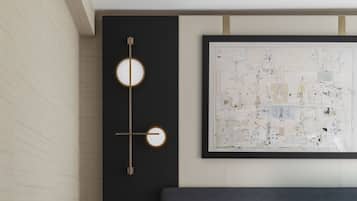 Una camera da letto moderna con un letto grande, un portalume a parete, una mappa astratta incorniciata e un piccolo comodino con una radio.