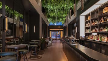 An indoor bar with a long counter, seating area, and a ceiling with green foliage.