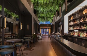 An indoor bar with a long counter, seating area, and a ceiling with green foliage.