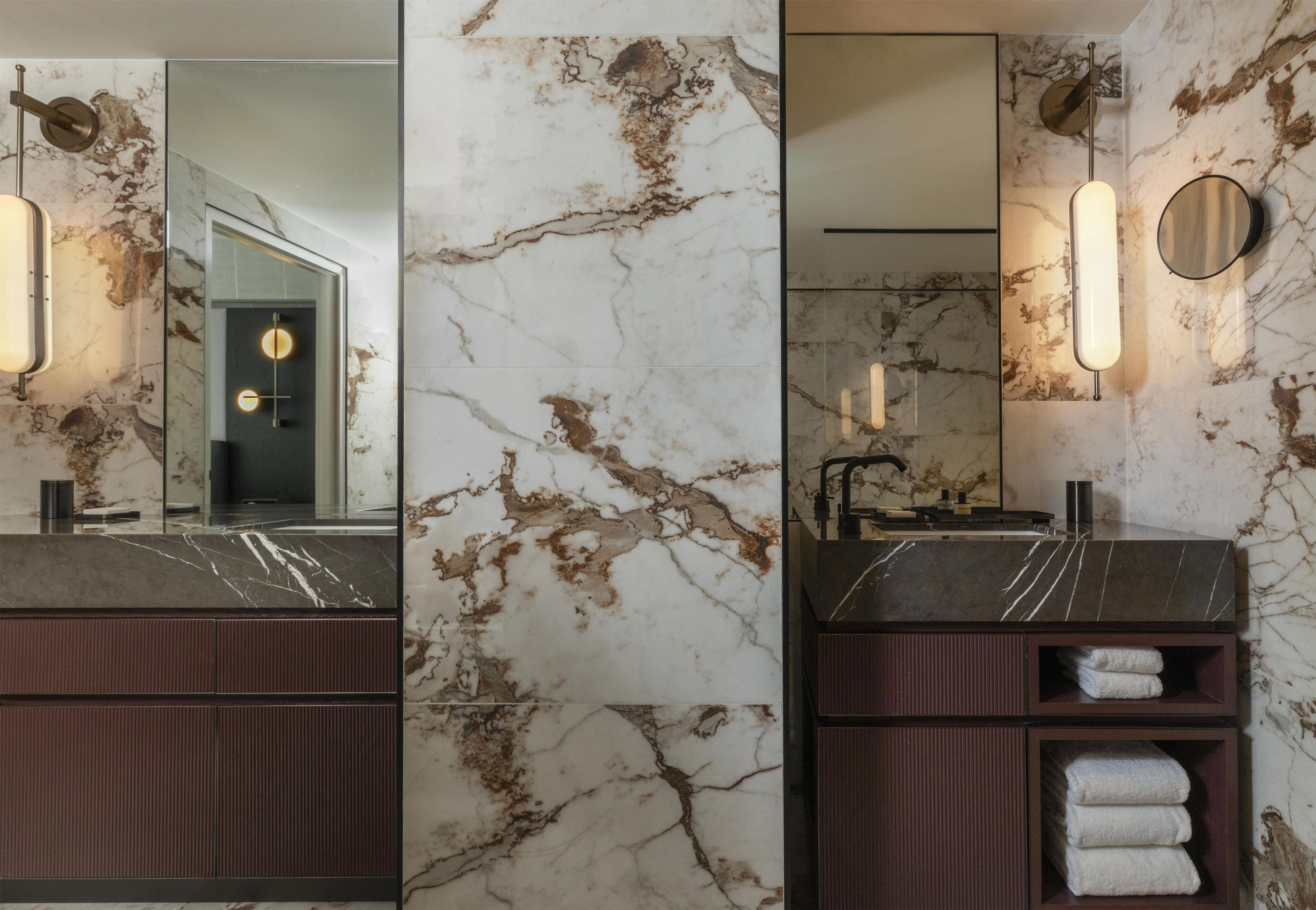 A bathroom with a marble vanity, a mirror, a towel rack, and a modern light fixture.