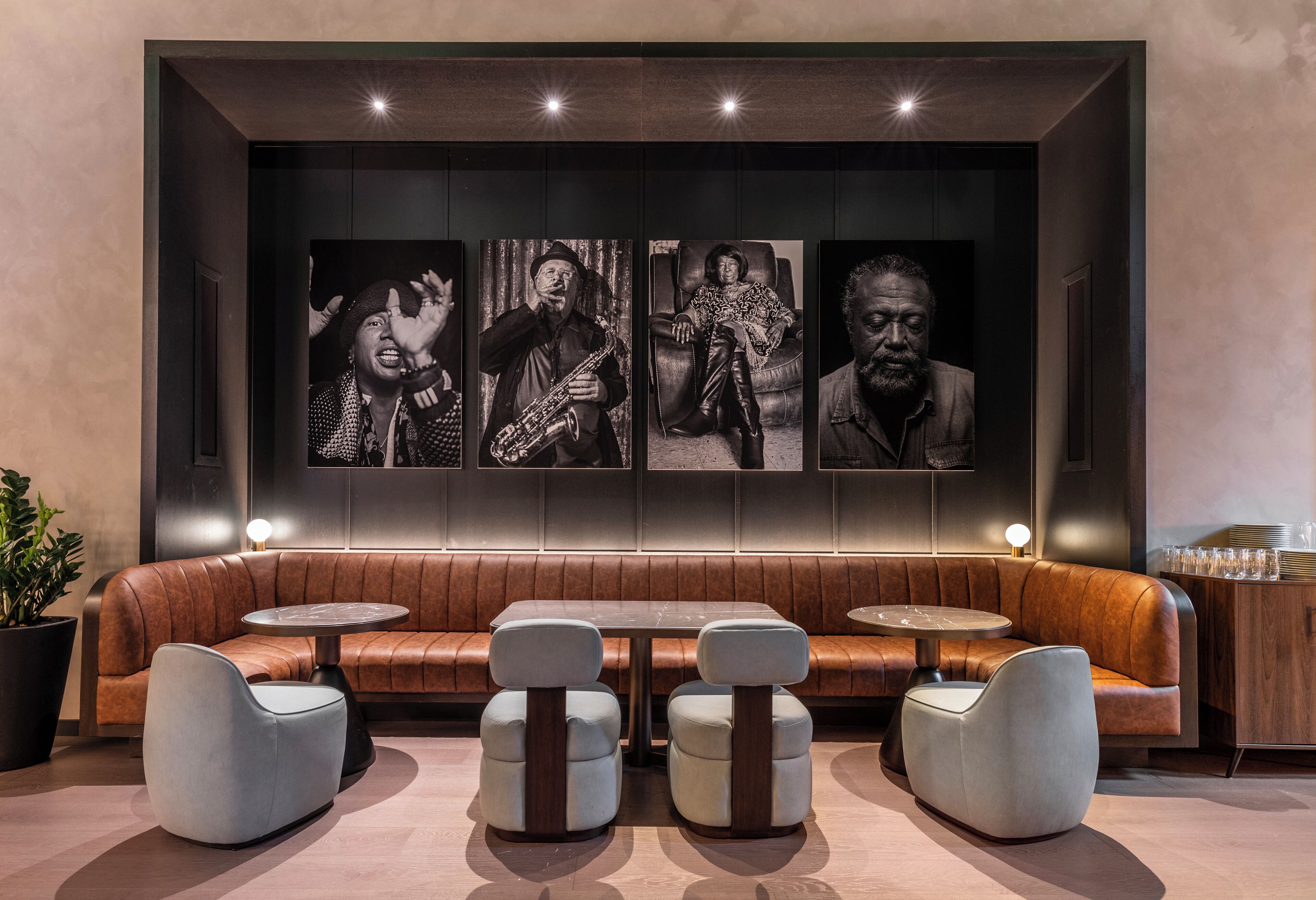 A modern lounge with a leather sofa, round tables, and a wall adorned with black-and-white photographs.