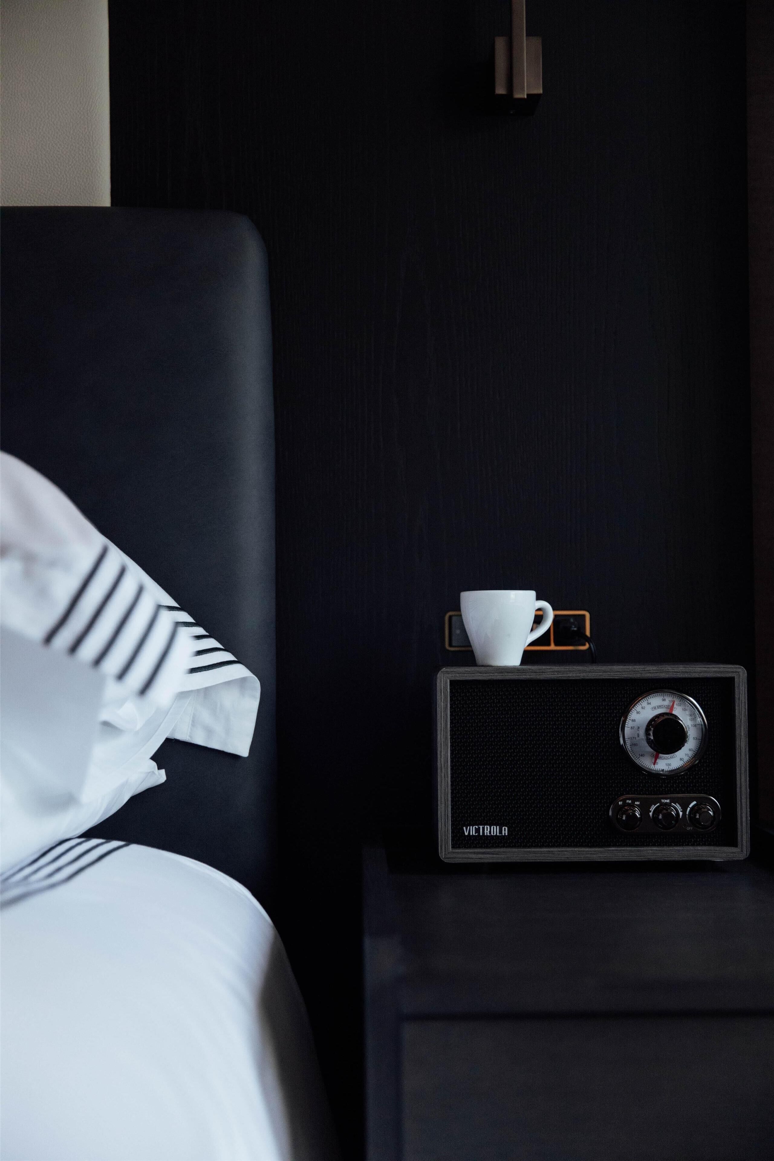 A bed with white linens, a white cup, and a vintage radio on a bedside table.