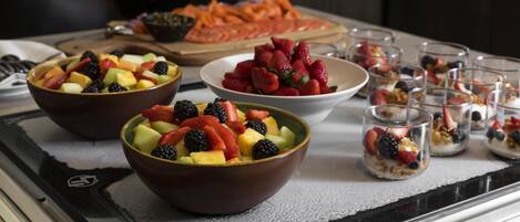 A breakfast buffet with bowls of fruit, a fruit platter, and small glasses of yogurt parfaits.