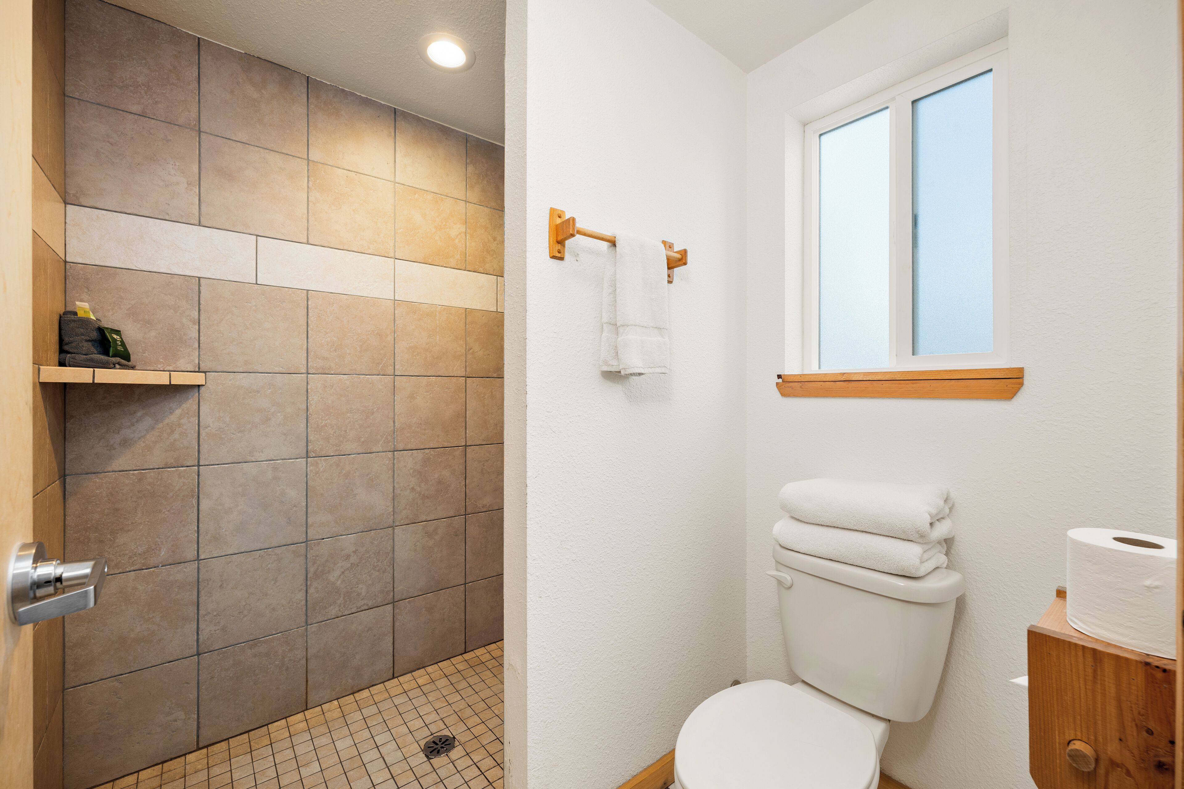 A bathroom with a shower area, a toilet, and a window.