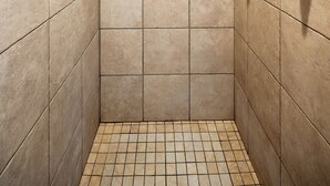 A small, tiled shower room with a handheld showerhead and a wall-mounted faucet.