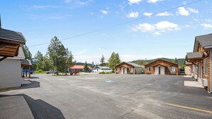 A parking lot with several wooden buildings, some with attached garages, and a few vehicles parked.