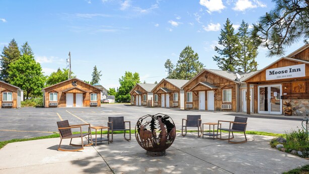 A row of log-style cabins with a sign for Moose Inn, outdoor seating, and a decorative metal sculpture.