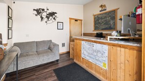 A room with a wooden reception desk, a grey sofa, a world map on the wall, and a framed map on the wall.