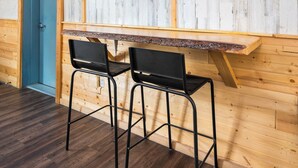 A room with a wooden wall, a blue door, and a TV mounted on the wall. There are two black chairs and a wooden table.