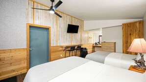 A hotel room with two beds, a desk with chairs, a TV, and a ceiling fan.