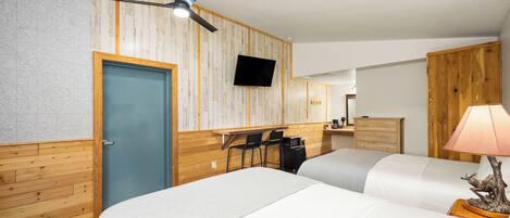 Een hotelkamer met twee bedden, een bureau met stoelen, een televisie en een plafondventilator.