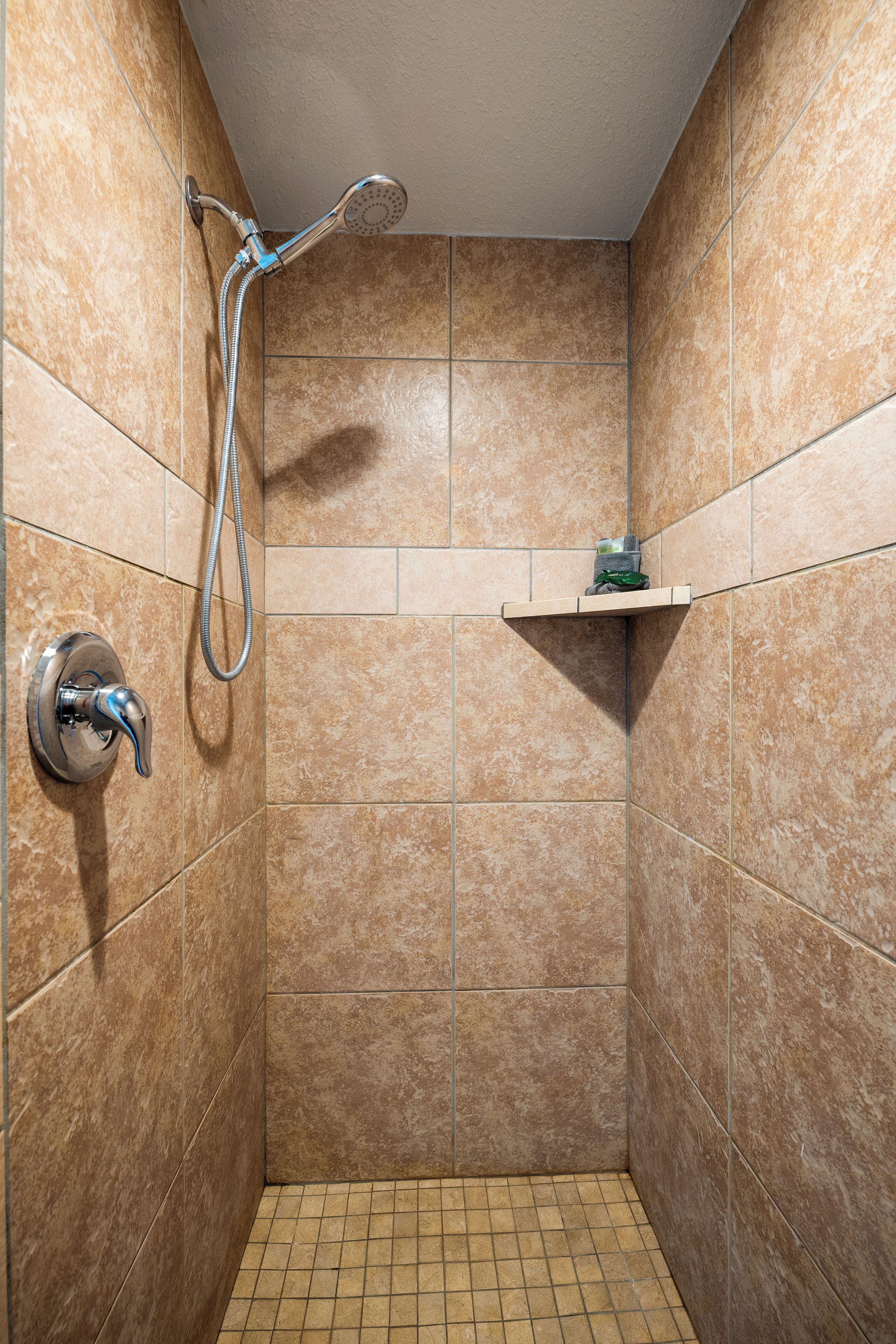 A small, tiled shower area with a handheld showerhead and a wall-mounted faucet.