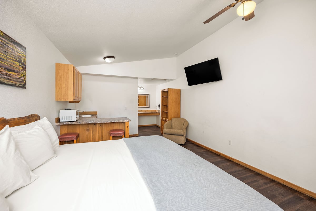 A bedroom with a bed, a desk, a chair, and a TV mounted on the wall.