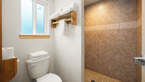 A bathroom with a toilet, a window, and a shower area with tiled walls.