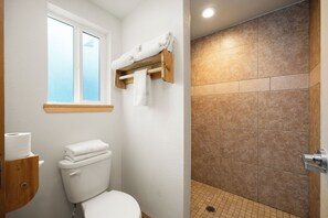 A bathroom with a toilet, a window, and a shower area with tiled walls.