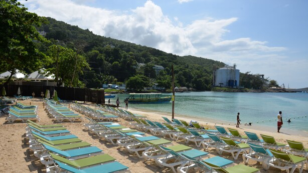 A beach with rows of sun loungers and a boat in the water. - Fisherman's Point Apartments (Ocho Rios)