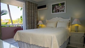 A bedroom with a bed, two bedside tables with lamps, a window with curtains, and a wall-mounted air conditioner. - Fisherman's Point Apartments (Ocho Rios)