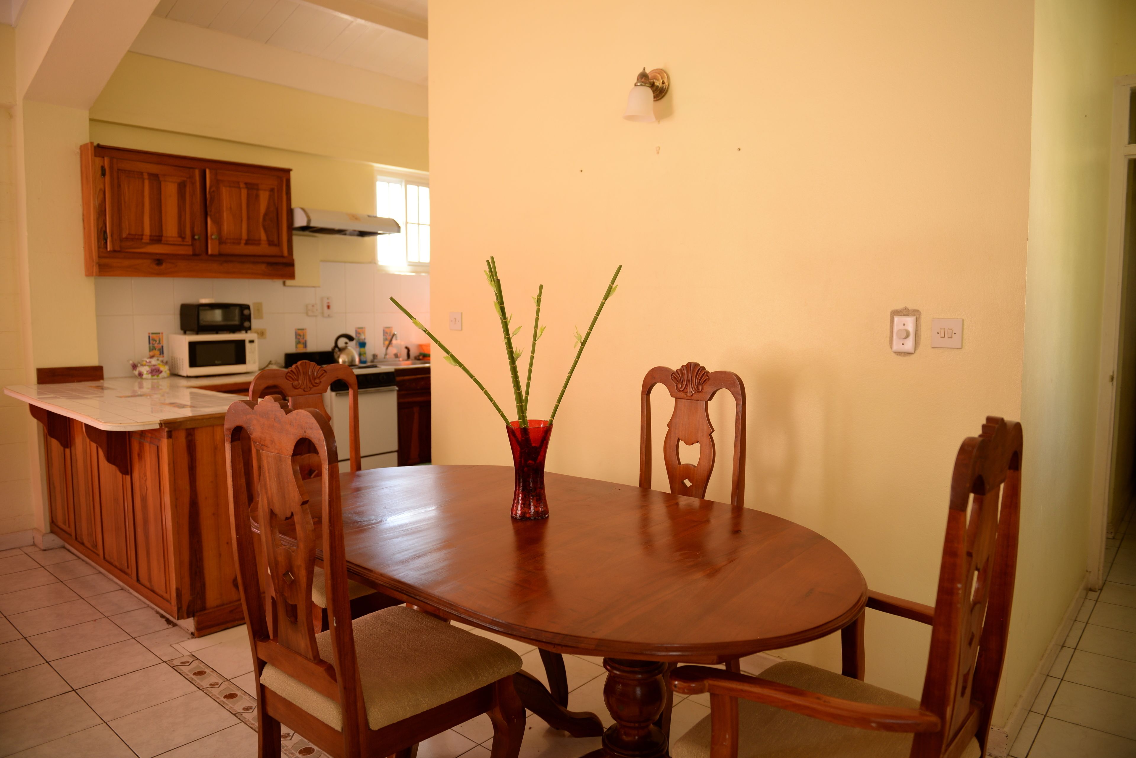 A dining area with a wooden table and chairs, a vase with plants, and a kitchen in the background.