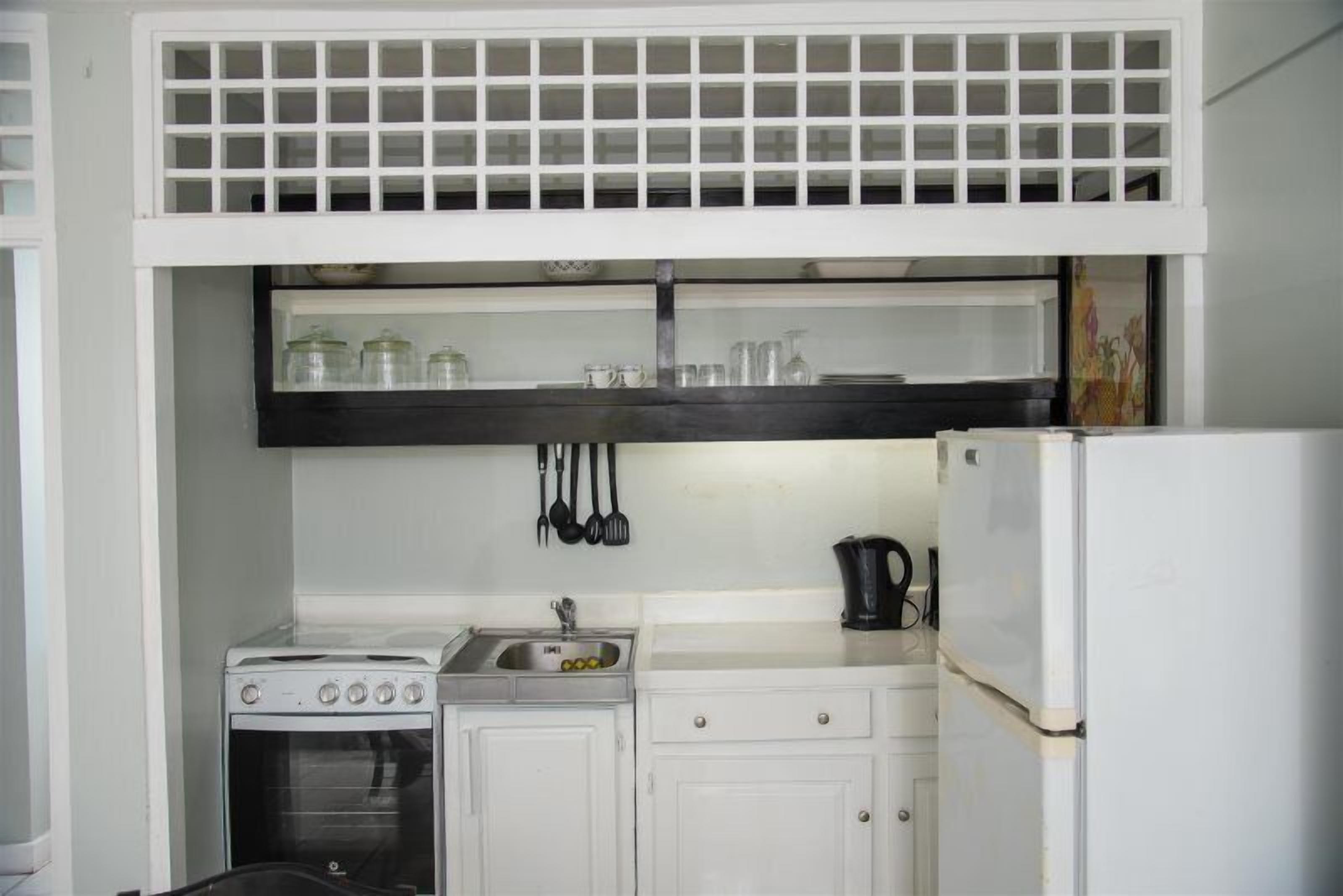 Una cuina compacta amb armaris blancs, forn de mur, rentatge i nevera.