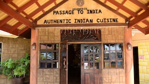 A wooden entrance with a sign reading "PASSAGE TO INDIA AUTHENTIC INDIAN CUISINE" and a potted plant beside it. - Fisherman's Point Apartments (Ocho Rios)