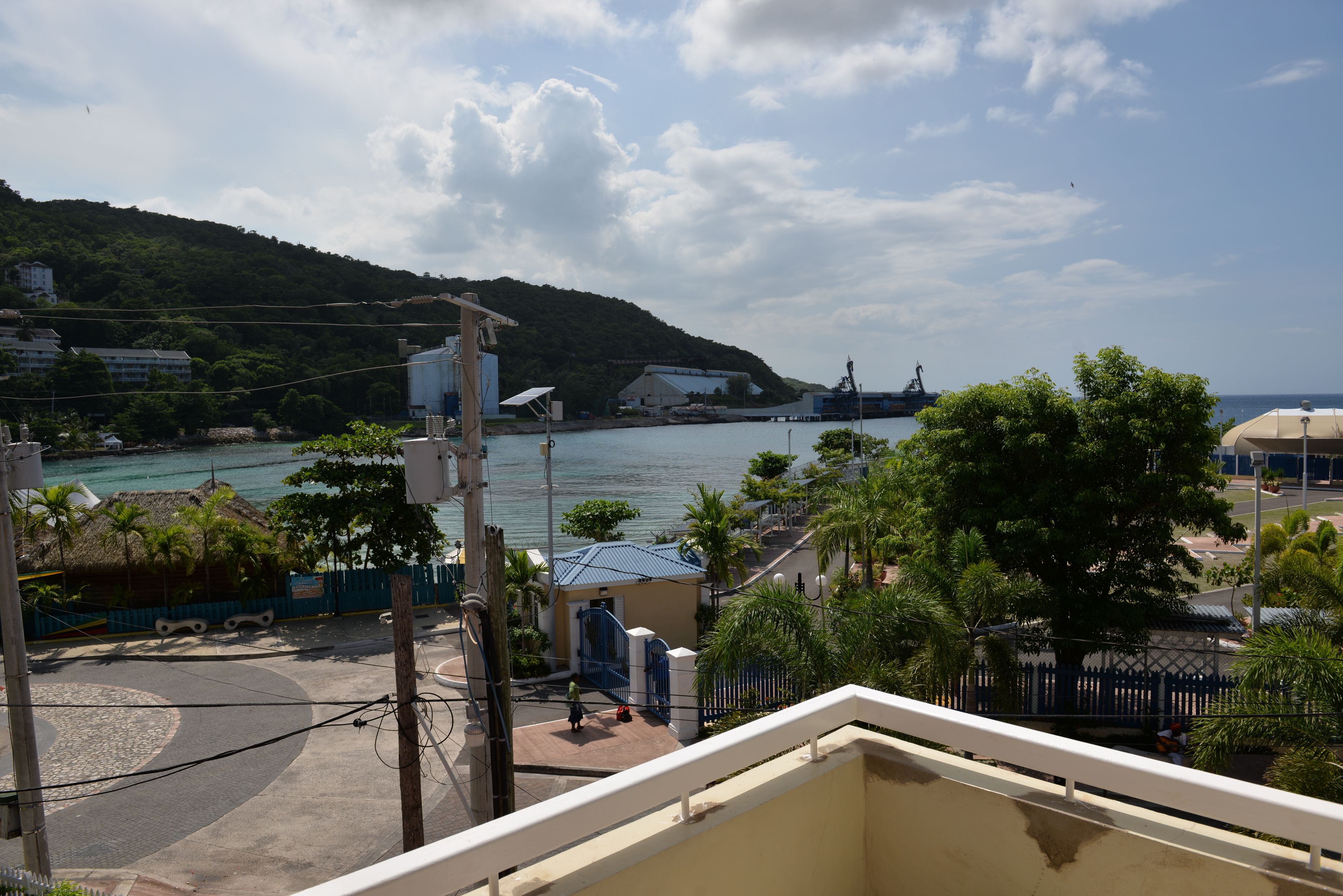 A coastal view with a beach, a hill, and buildings in the background.