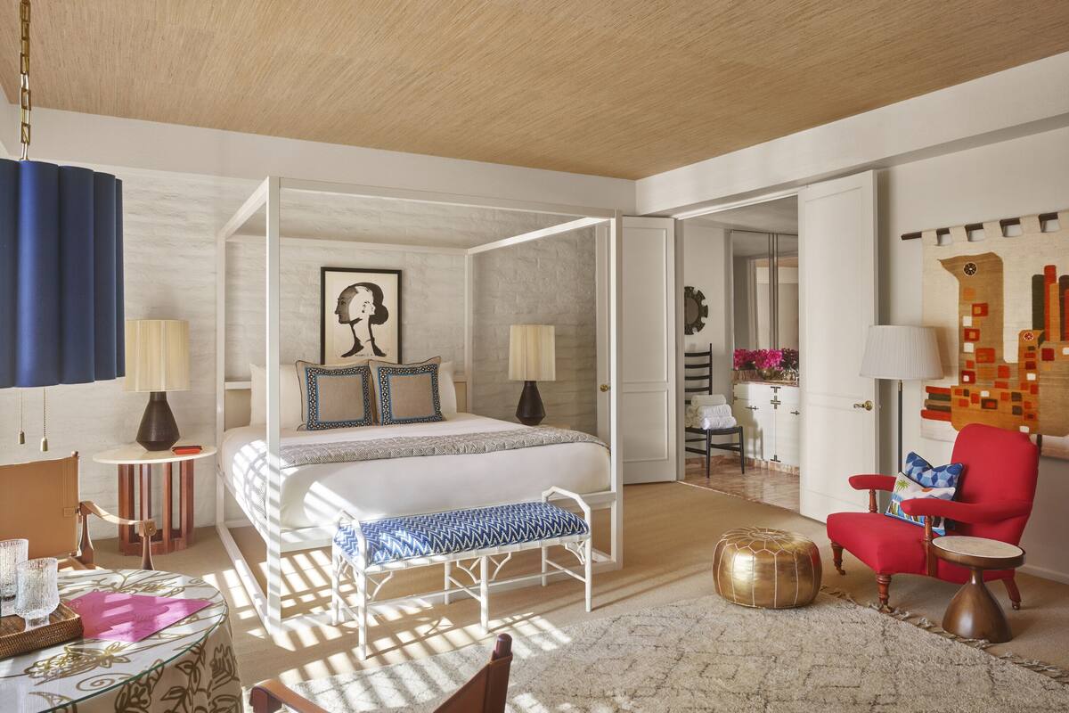 Ein geräumiges Schlafzimmer mit einem großen Bett, Nachttischen, einem roten Sessel und Blick ins Bad.
