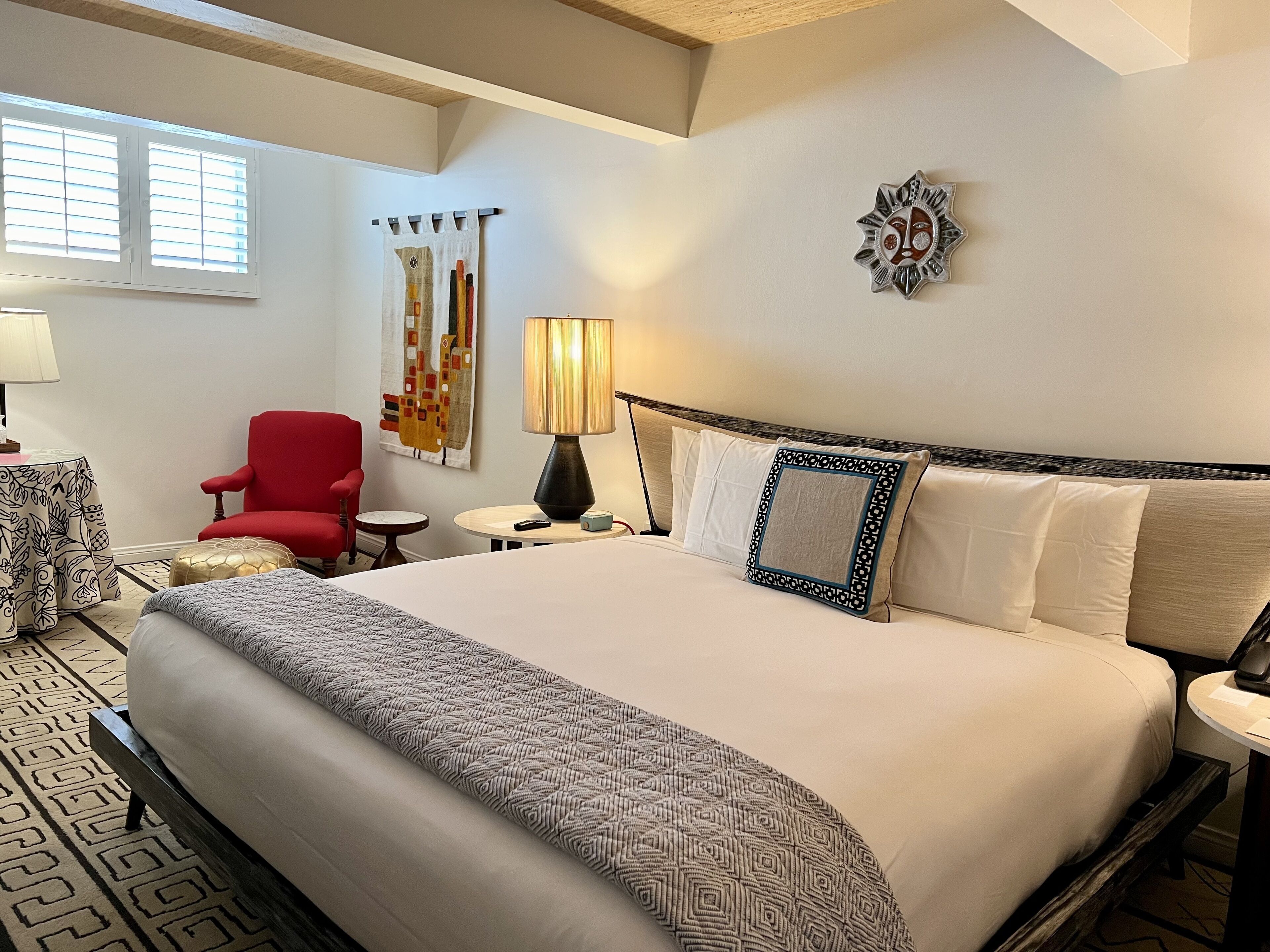 Une chambre d’hôtel avec un grand lit, un fauteuil rouge, une petite table ronde, une lampe et un élément de décoration murale.