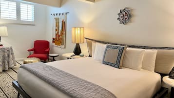 Une chambre d’hôtel avec un grand lit, un fauteuil rouge, une petite table ronde, une lampe et un élément de décoration murale.