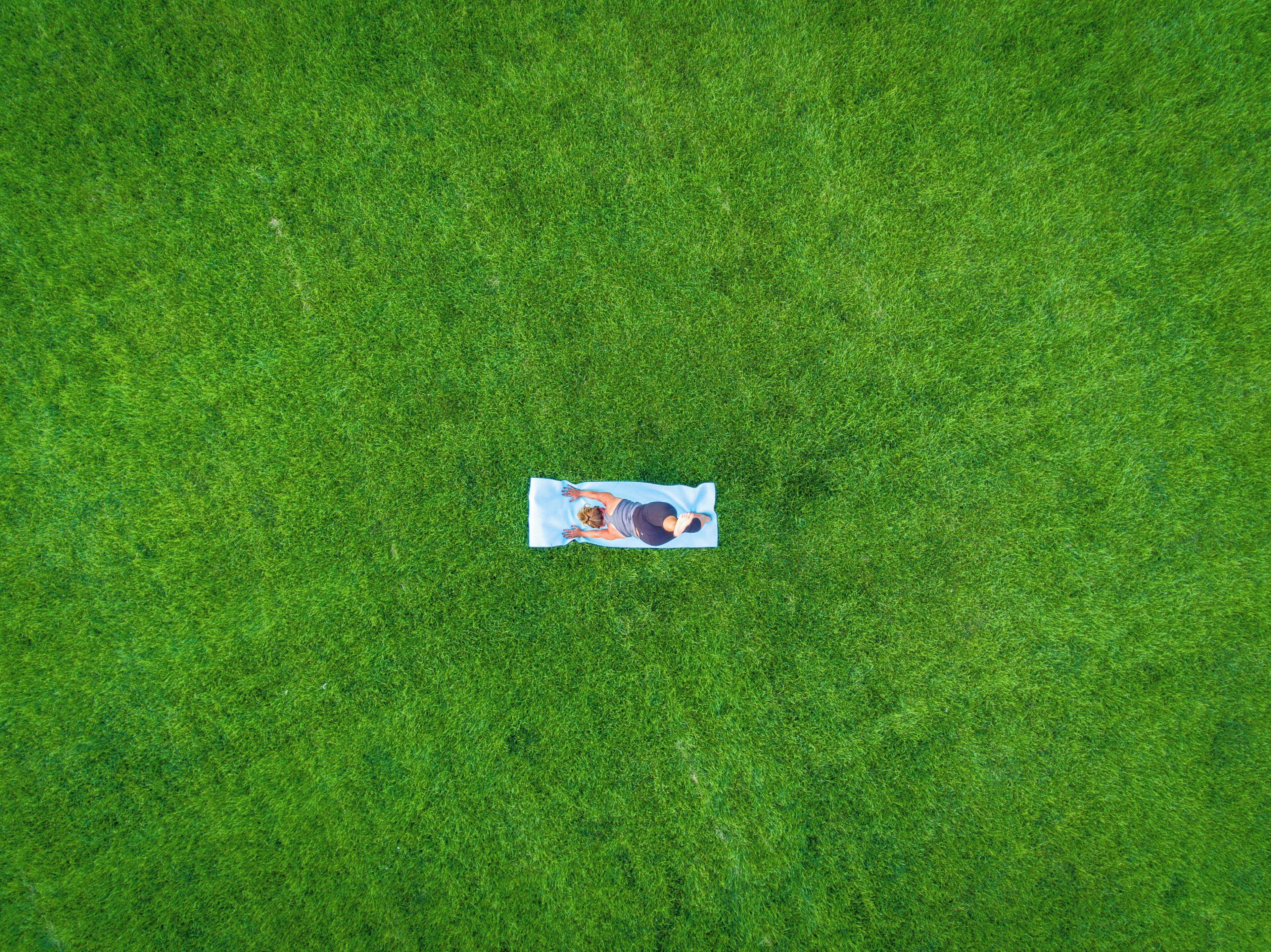 A person lying on a blue mat on a grassy field.