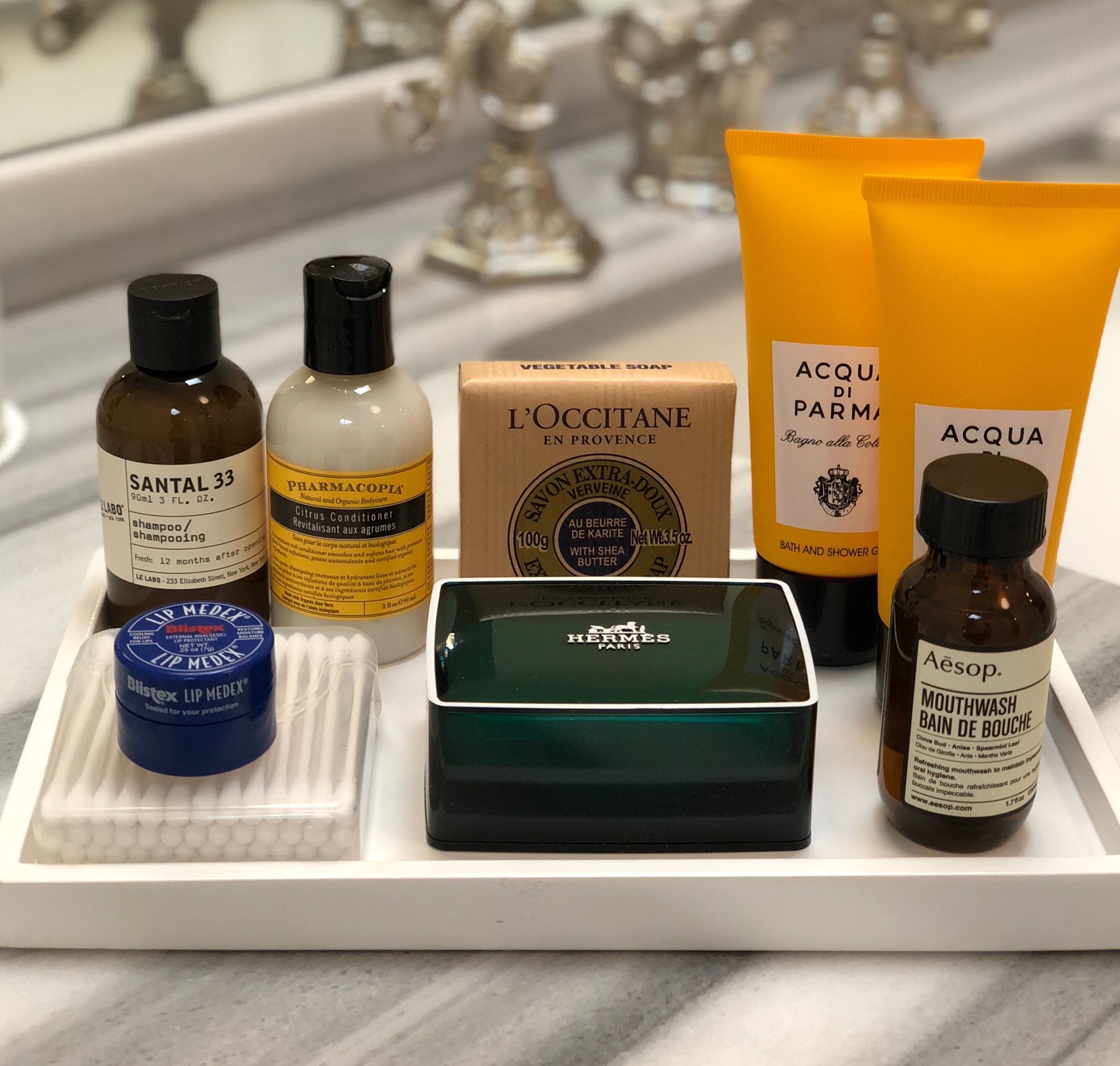 A variety of toiletries including Santal 33, PHARMACOPIA, L'OCCITANE, ACQUA, and Aesop products.