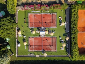 A tennis court complex with two courts, seating areas, and surrounding greenery. - Parker Palm Springs (Palm Springs)