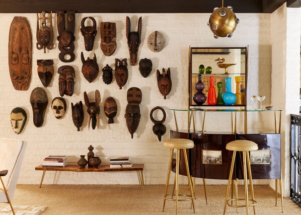A room with a wall of wooden masks, a glass shelf with decorative items, and a vintage-style bar area.