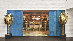 Zona de bar con una puerta decorativa azul, detalles dorados y suelo de mármol.