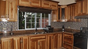 Cucina con mobili in legno, un piano di lavoro in granito, un fornello nero e una finestra vista verde.