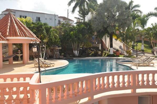 A pool area with lounge chairs, a gazebo, and palm trees. - Sun Rise Condos By The Vacation Casa (Tower Isle)