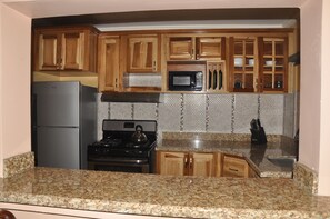 A kitchen with wooden cabinets, a stainless steel refrigerator, a microwave, and a gas stove. - Sun Rise Condos By The Vacation Casa (Tower Isle)