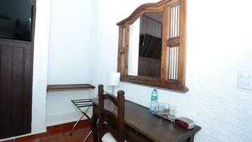 Una habitación pequeña y limpia con una mesa de madera, una silla, un espejo, un reloj y una botella de agua.