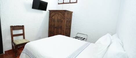 A bedroom with a bed, a wooden wardrobe, a chair, and a television mounted on the wall.