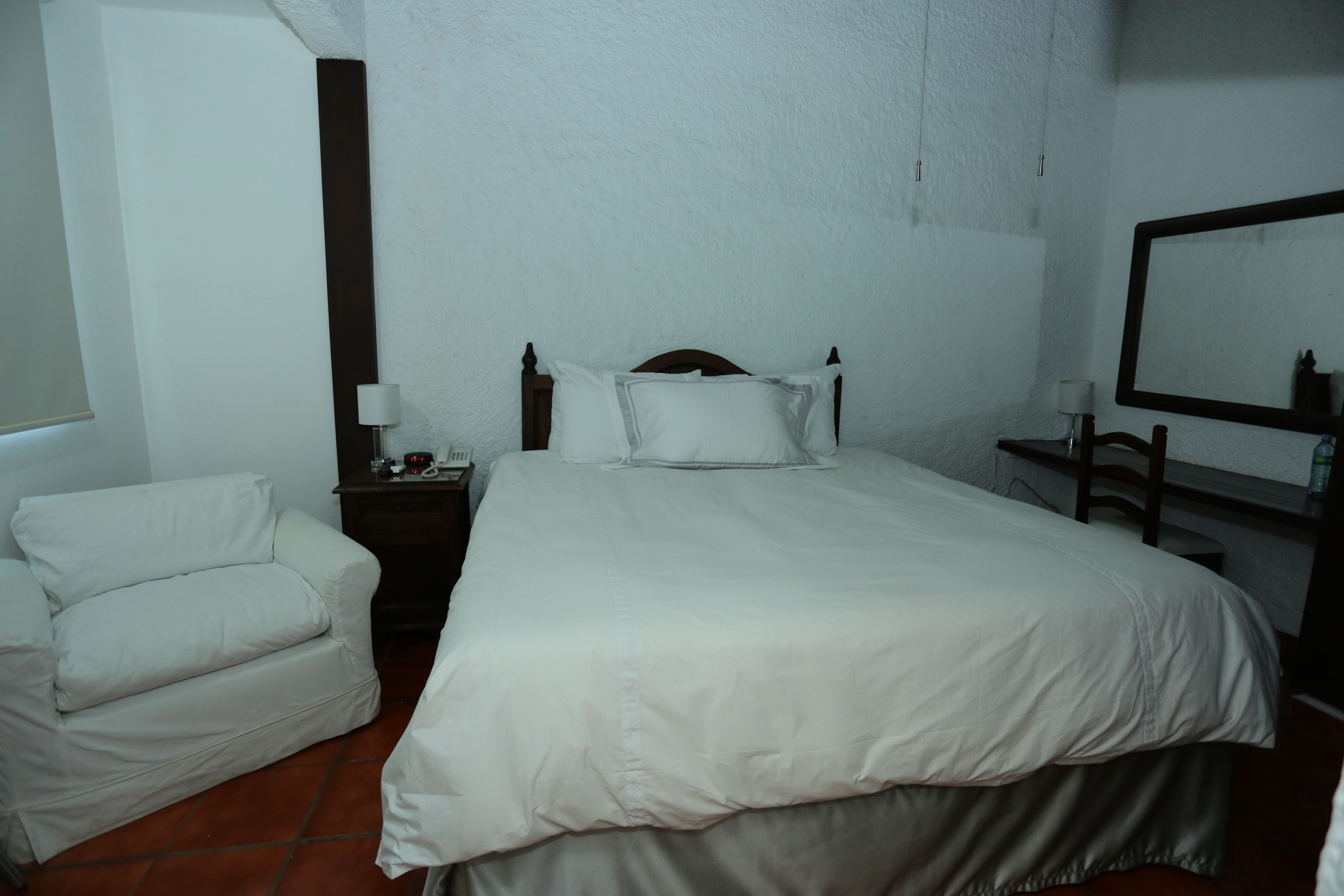 Ein Hotelzimmer mit einem großen Bett, einem Nachttisch mit Lampe, einem Sessel und einem Spiegel an der Wand.