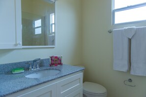 A bathroom with a white sink, a mirror, a window, and a toilet. - Draxhall Manor Holiday Homes (Ocho Rios)