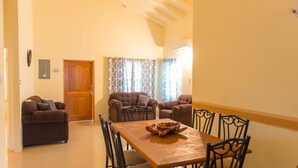 Un área de comedor con una mesa y sillas de madera, un sofá marrón y cortinas estampadas.