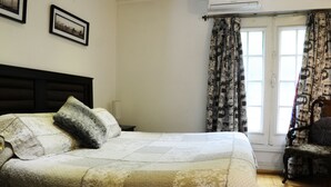 A neatly made bed with a patterned bedspread, a dark headboard, and a chair with a patterned cushion.