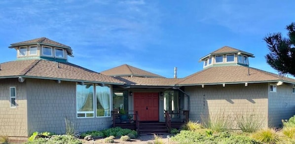 A two-story house with a red front door, a covered porch, and a small attic window on the roof.