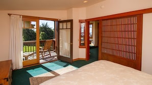 A bedroom with a large bed, a sliding glass door to a balcony, a wooden shoji screen, and a small window with a clock. - Mendocino View East (Mendocino)