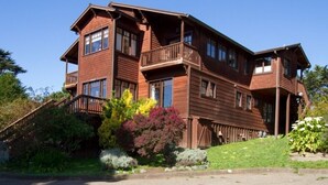 A two-story wooden house with a balcony, surrounded by lush greenery and a stone staircase. - Mendocino View East (Mendocino)