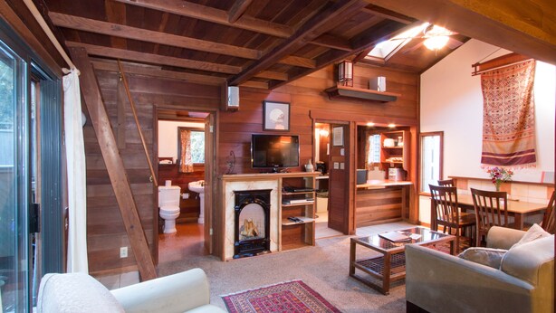 A cozy living room with a fireplace, wooden beams, a television, and comfortable seating.